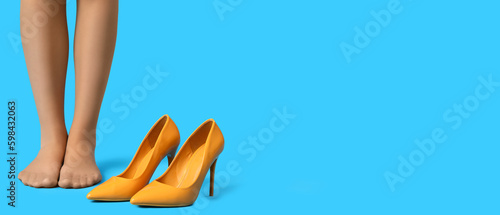 Legs of barefoot woman standing near stylish high-heeled shoes on light blue background with space for text