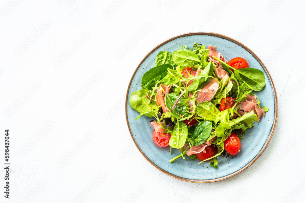 Green salad with fresh leaves, tomatoes and jamon at white table. Top view with copy space. Green salad with fresh leaves, tomatoes and jamon at white table. Top view with copy space.