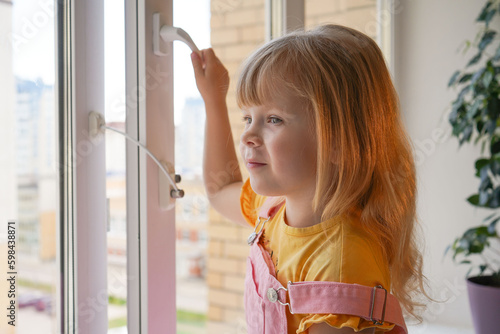 safety at home for small children. a lock on the window protects children from opening the window. The girl 4 years old tries to open the window standing on the windowsill on a high floor.