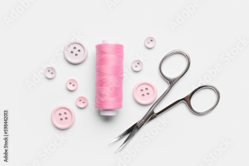 Composition with thread spool, scissors and buttons on light background