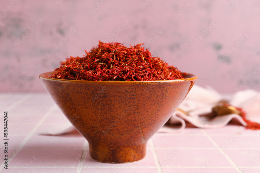 Bowl with pile of saffron on pink tile background Bowl with pile of saffron on pink tile background