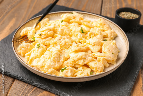 Plate of delicious scrambled eggs with spices on brown wooden background, closeup