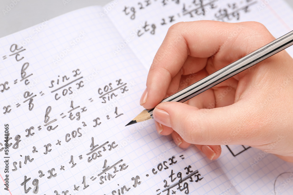 Woman writing maths formulas in copybook with pencil, closeup Woman writing maths formulas in copybook with pencil, closeup