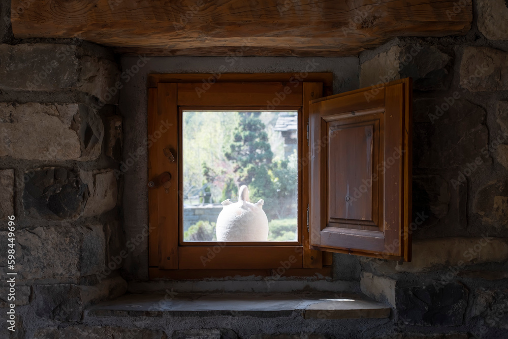 a white botijo seen from the inside of a window of a stone village house with wooden shutters, typical spanish clay botijo to keep the water cool in summer, rustic atmosphere