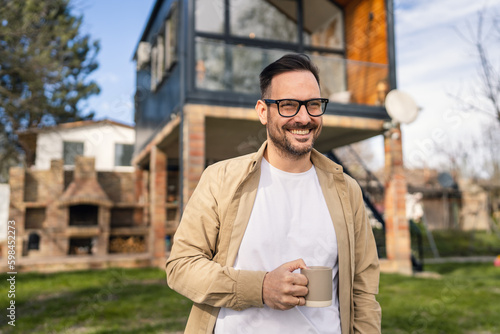 Happy Homeowner Man with Cup of Tea Stand in Front of Modern House