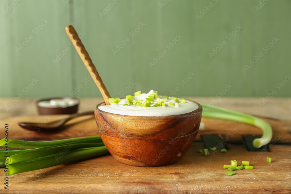 Bowl with sour cream and sliced green onion on brown wooden table near green wall Bowl with sour cream and sliced green onion on brown wooden table near green wall