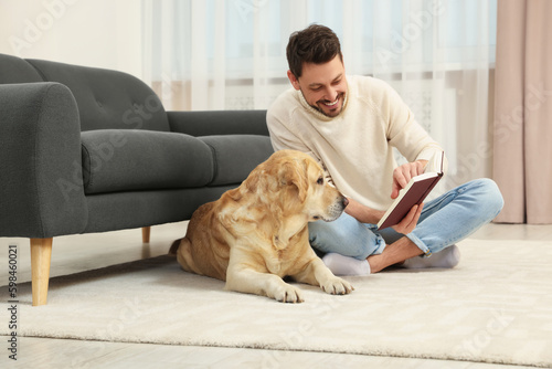 Man reading book on floor near his cute Labrador Retriever at home