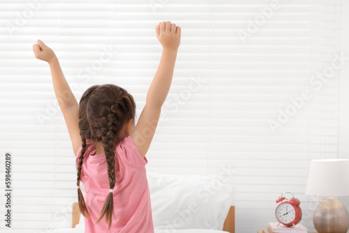 Cute little girl stretching in cosy bedroom, back view