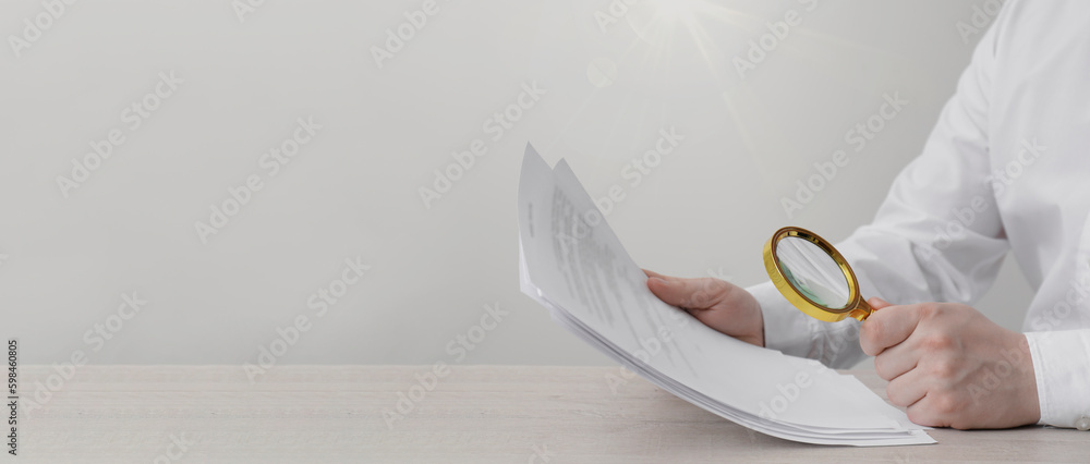 Man looking at documents through magnifier at wooden table, closeup. Banner design with space for text