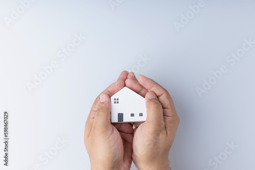 Real estate investing concepts, finance, banking, and saving money. A little wooden house model in hand, white background with copy space. Business of residence can make a profit in the future.