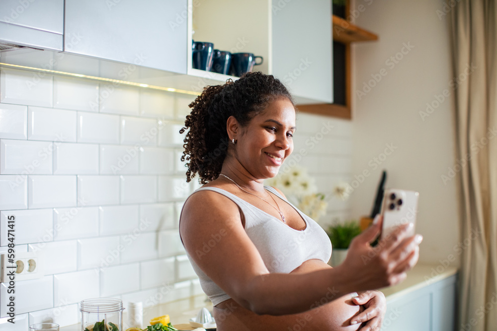 Young pregnant latina woman using a smart phone and having a video call while in the kitchen of a house Young pregnant latina woman using a smart phone and having a video call while in the kitchen of a house