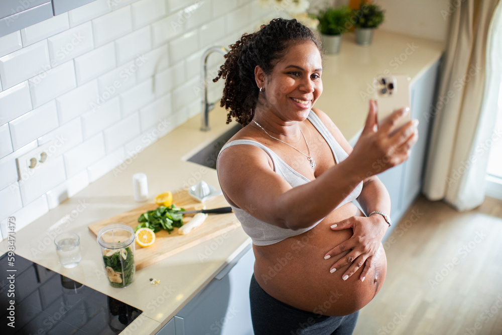 Young pregnant latina woman using a smart phone and having a video call while in the kitchen of a house Young pregnant latina woman using a smart phone and having a video call while in the kitchen of a house