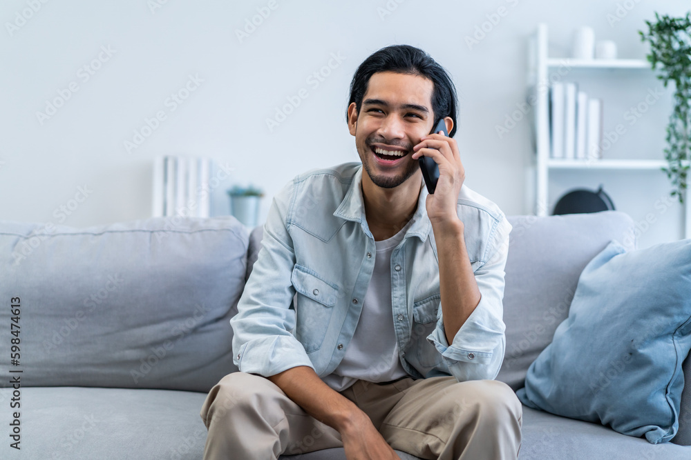 Asian attractive man sit on sofa and talking on mobile phone in house. Asian attractive man sit on sofa and talking on mobile phone in house.