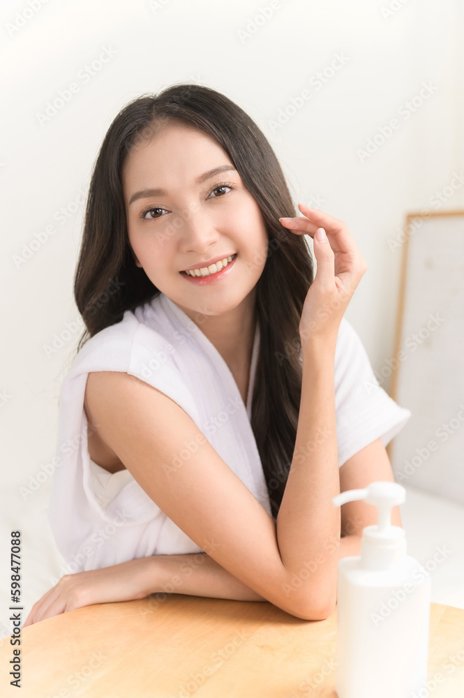 Close up portrait photo of young beautiful Asian woman taking care of her facial skin after apply face skin care cosmetic lotion moisturizer product and checking in mirror at home. Beauty care concept Close up portrait photo of young beautiful Asian woman taking care of her facial skin after apply face skin care cosmetic lotion moisturizer product and checking in mirror at home. Beauty care concept
