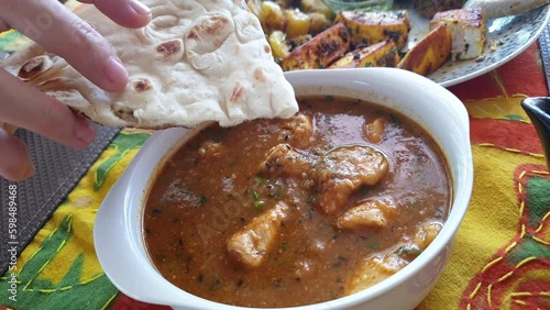 Woman hand dipping nann in Indian chicken curry eating traditional India food with potato and cheese on side photo