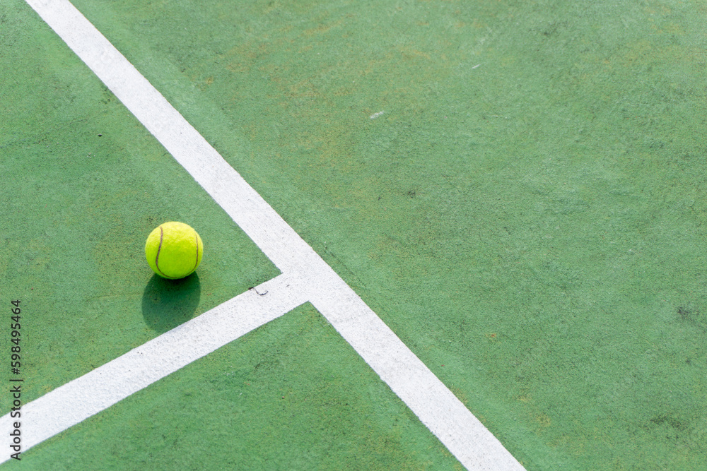 Yellow tennis ball on green court and white lines. Top angle view of tennis ball on court.