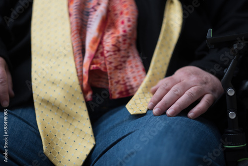 Wearing a colorful scarf and a yellow tie, a disabled transman in his powerchair expresses pride and mobility.