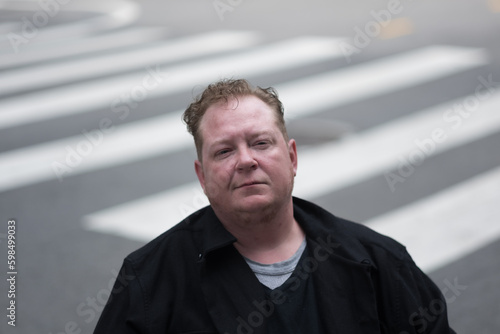 With zebra stripes fading into the background, a disabled transman in a powerchair pauses in a crosswalk to express accessible design as a life-changing justice issue.