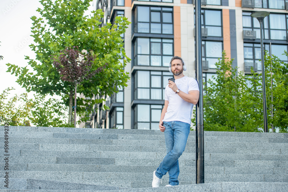 photo of man in music headphones with coffee cup. man in music headphones outdoor.