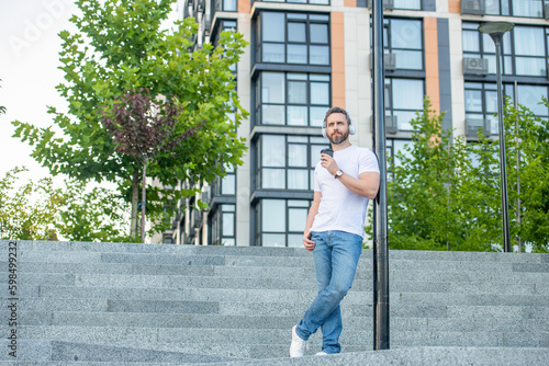 photo of man in music headphones with coffee cup. man in music headphones outdoor.