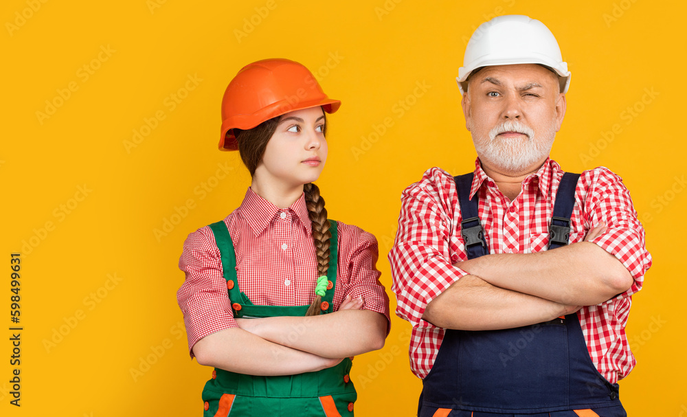 serious child and grandfather builder in helmet on yellow background serious child and grandfather builder in helmet on yellow background