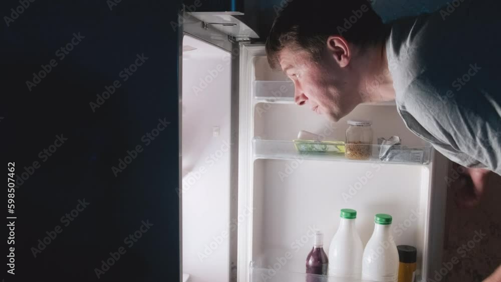 Caucasian hungry man at night open fridge searching food. Happy male on diet with night hunger taking and eating apple from refrigerator Generative AI Caucasian hungry man at night open fridge searching food. Happy male on diet with night hunger taking and eating apple from refrigerator Generative AI