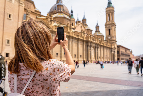 Tourist woman taking a photo with the mobile phone to the cathedral basilica del Pilar in Zaragoza, Spain.