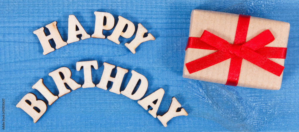 Fototapeta premium Wrapped gift with red ribbon for birthday. Inscription happy birthday on boards