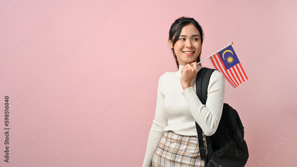 Cheerful young Asian woman showing a Malaysia flag on pink isolated background Cheerful young Asian woman showing a Malaysia flag on pink isolated background