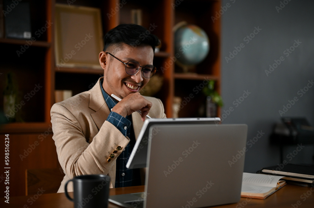 Professional and happy adult Asian businessman working on his business project on tablet Professional and happy adult Asian businessman working on his business project on tablet
