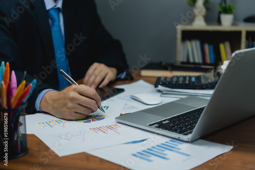 Business man holding pen with analysis financial graph and report marketing statistic chart on desk.