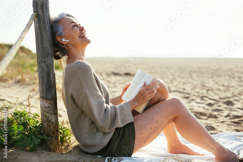 Happy mature woman with book sitting at beach photo