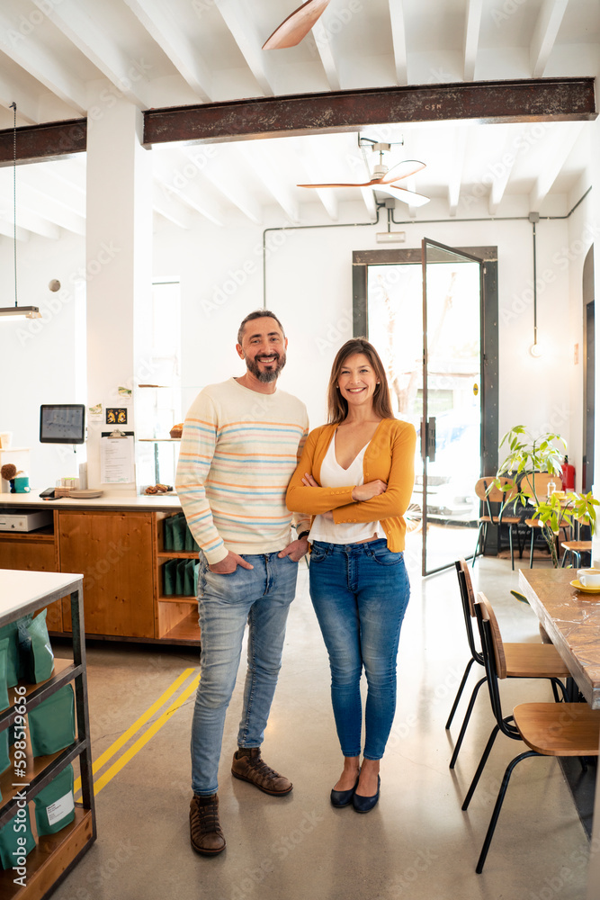 Smiling woman with arms crossed standing by owner at cafe Smiling woman with arms crossed standing by owner at cafe