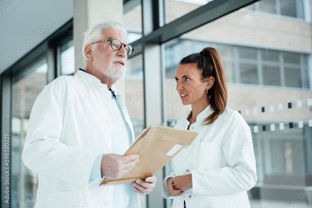 Senior doctor holding document and discussing with colleague in hospital Senior doctor holding document and discussing with colleague in hospital