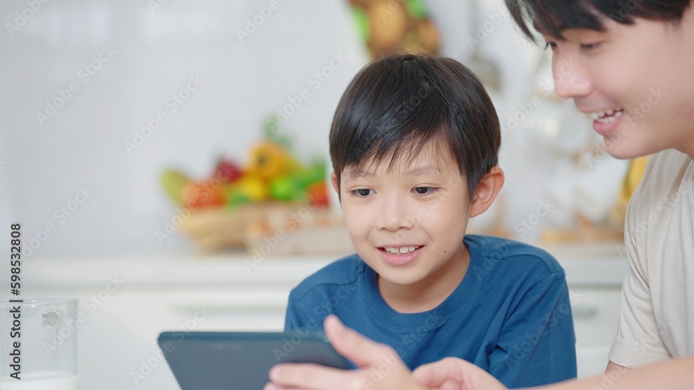Asian father teaching little son using digital tablet for learning online at home in social distancing during self quarantine. Online education concept Asian father teaching little son using digital tablet for learning online at home in social distancing during self quarantine. Online education concept