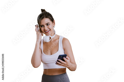 Fototapeta Naklejka Na Ścianę i Meble -  Cheerful brunette girl in sportswear holds phone smiles checking sound of new headphones against transparent background. Fit caucasian young woman makes call during break of exercise. Sport, fitness.