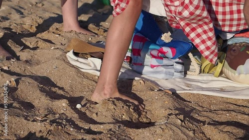 The boy, covered with a towel, changing his wet swimsuit to dry clothes. Legs closeup on a sandy beach