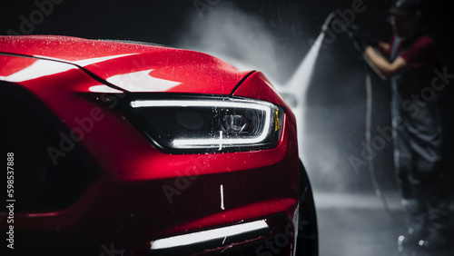 Advertising Style Photo of a Professional Car Wash Specialist Using a High Pressure Washer to Clean and Prepare a Red Sports Coupe for Detailing, Polishing and Waxing