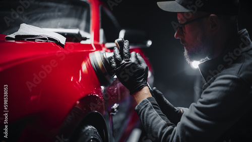 Car Ad Style Photo of a Professional Car Detailer Using an Electric-Powered Polishing Machine to Work on a Fender of a Beautiful Red Sportscar After Washing and Detailing the Vehicle photo