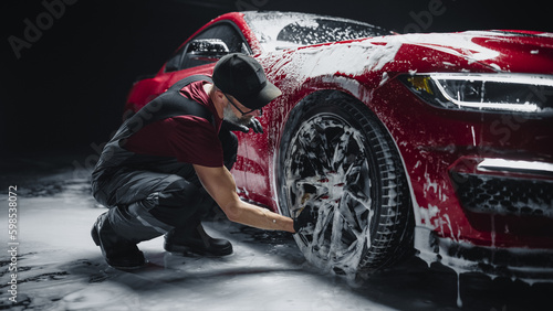 Red Sportscar's Wheels Covered in Shampoo Being Rubbed by a Soft Sponge at a Stylish Dealership Car Wash. Performance Vehicle Being Washed in a Detailing Studio © Gorodenkoff