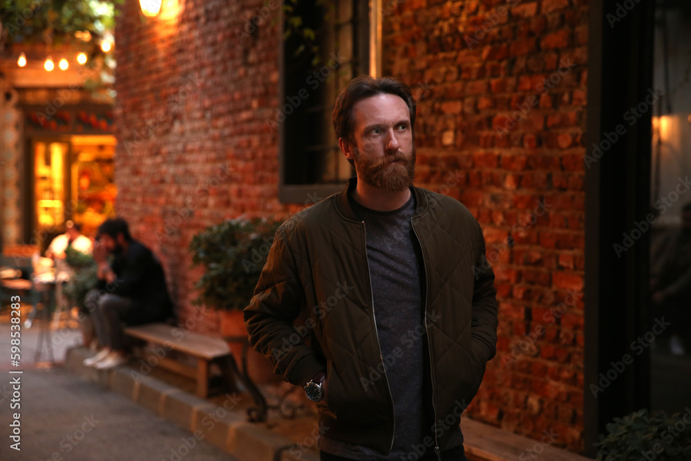 Bearded Caucasian man posing in front of a blurry red stone wall