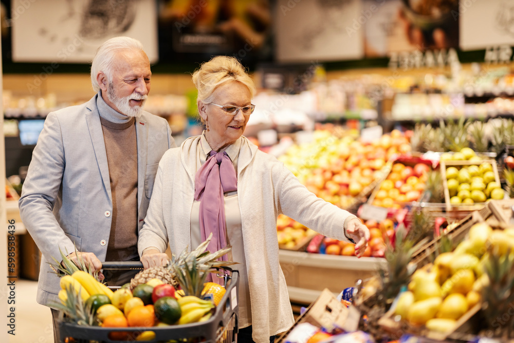 An old healthy couple is purchasing fresh fruits at the supermarket.