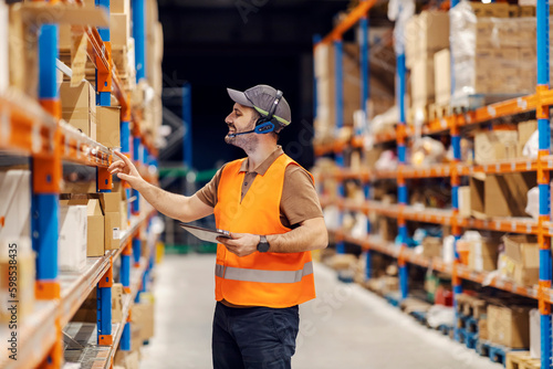 A post office manager is using tablet while searching for shipment in storage.