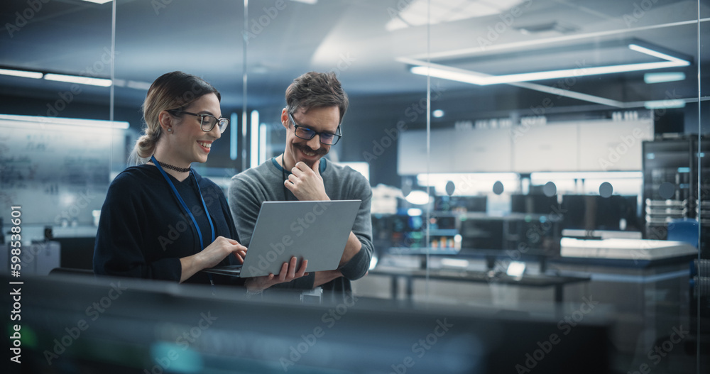 Portrait of Two Creative Young Female and Male Engineers Using Laptop Computer to Analyze and Discuss How to Proceed with the Artificial Intelligence Software. Standing in High Tech Research Office - obrazy, fototapety, plakaty 