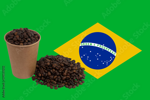 A disposable paper cup filled with coffee beans and a bunch of coffee beans against the background of the flag of Brazil (close-up). The largest exporter of coffee in the world. Brazilian coffee