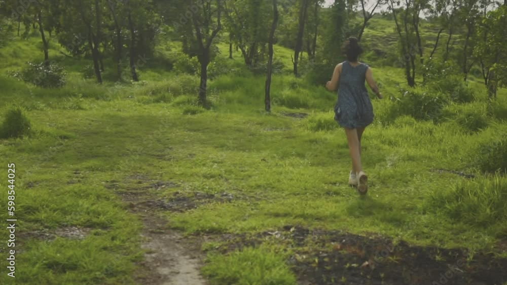 Women in blue dress running towards the trees in an open grassy woodland on a warm spring day Women in blue dress running towards the trees in an open grassy woodland on a warm spring day