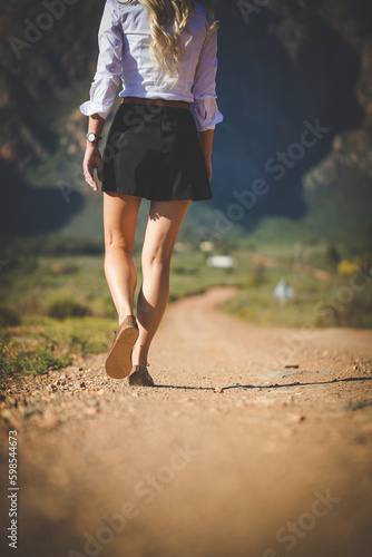 Close up image of a pretty woman with muscular legs walking on a dirt road wearing handmade leather shoes.