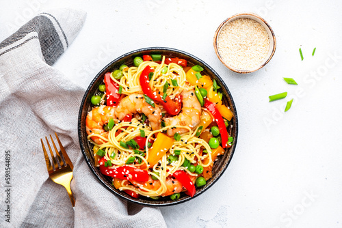 Stir fry noodles with shrimps, paprika, green pea, chives and sesame seeds in bowl. Asian cuisine dish. White kitchen table background, top view