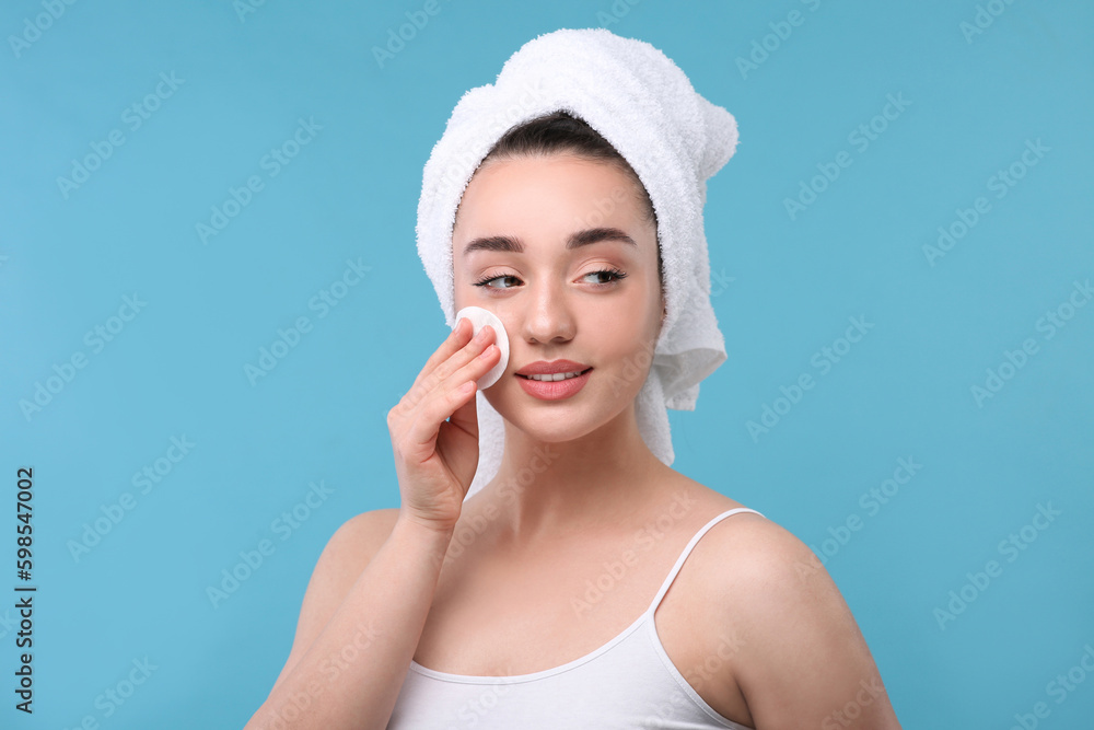 Beautiful woman in terry towel removing makeup with cotton pad on light blue background Beautiful woman in terry towel removing makeup with cotton pad on light blue background