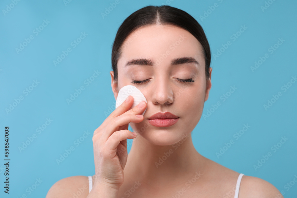 Beautiful woman removing makeup with cotton pad on light blue background Beautiful woman removing makeup with cotton pad on light blue background